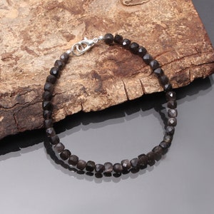 May include: A black gemstone bracelet with a silver clasp. The bracelet is made of faceted beads and is strung on a silver chain.