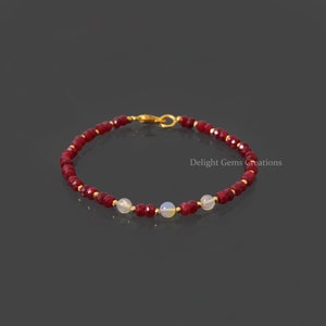 May include: A red gemstone beaded bracelet with three white opal beads and a gold clasp.  Delight Gems Creations.