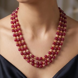 Può includere: Collana a più fili con perline rosse e color pesca alternate. La collana è a strati, con ogni filo che scende a cascata lungo la scollatura. Le perline hanno un aspetto liscio e lucido, creando un look classico ed elegante.