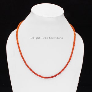 May include: A necklace made of small, round, orange carnelian beads. The necklace is displayed on a white mannequin bust. The text "Delight Gems Creations" is visible on the bust.