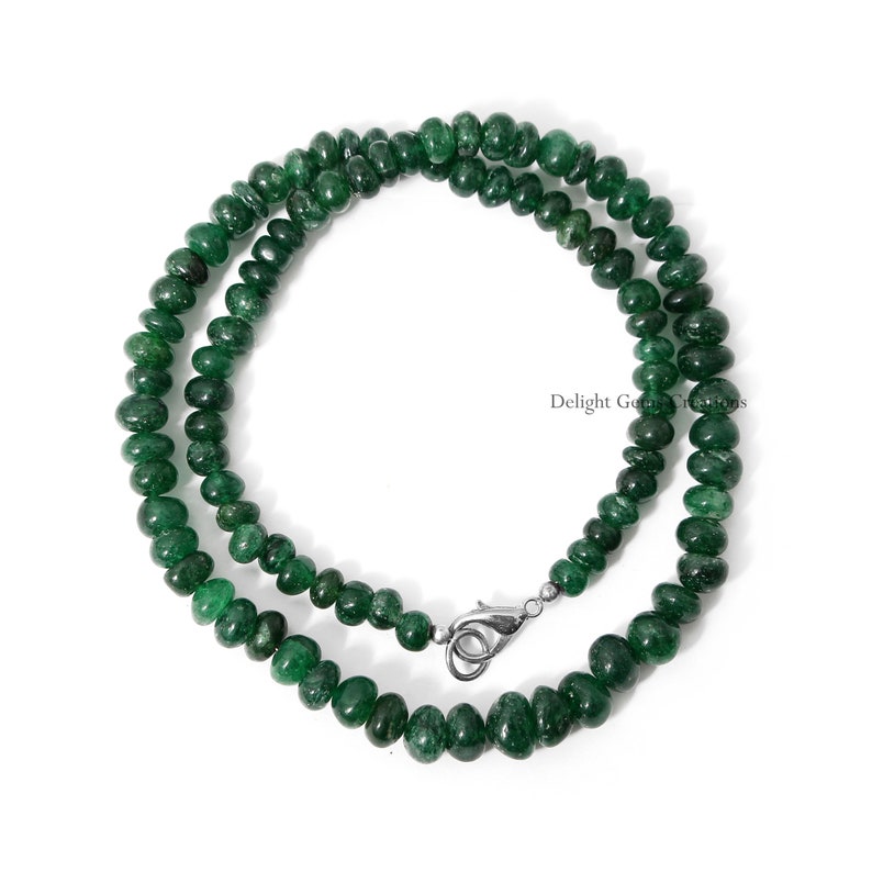 Puede incluir: Un collar compuesto por peque&ntilde;as piedras preciosas redondas de color verde oscuro. Las cuentas est&aacute;n ensartadas, formando una doble hebra con un cierre plateado. El collar se muestra sobre un fondo blanco.
