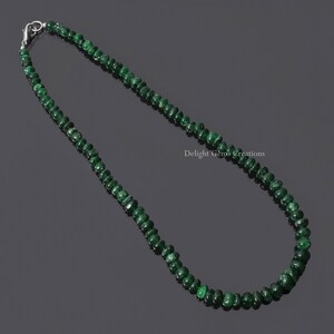 Puede incluir: Un collar compuesto por peque&ntilde;as cuentas redondas de color verde oscuro. Las cuentas est&aacute;n ensartadas con un cierre plateado. El collar se muestra sobre un fondo oscuro. El texto "Delight Gems Creations" es visible.