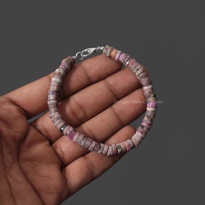 May include: A pink and gray gemstone bracelet with a silver clasp. The bracelet is made of small, round beads.