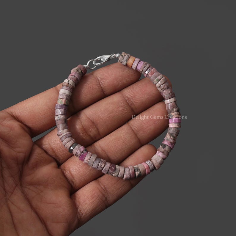 May include: A pink and gray gemstone bracelet with a silver clasp. The bracelet is made of small, round beads.