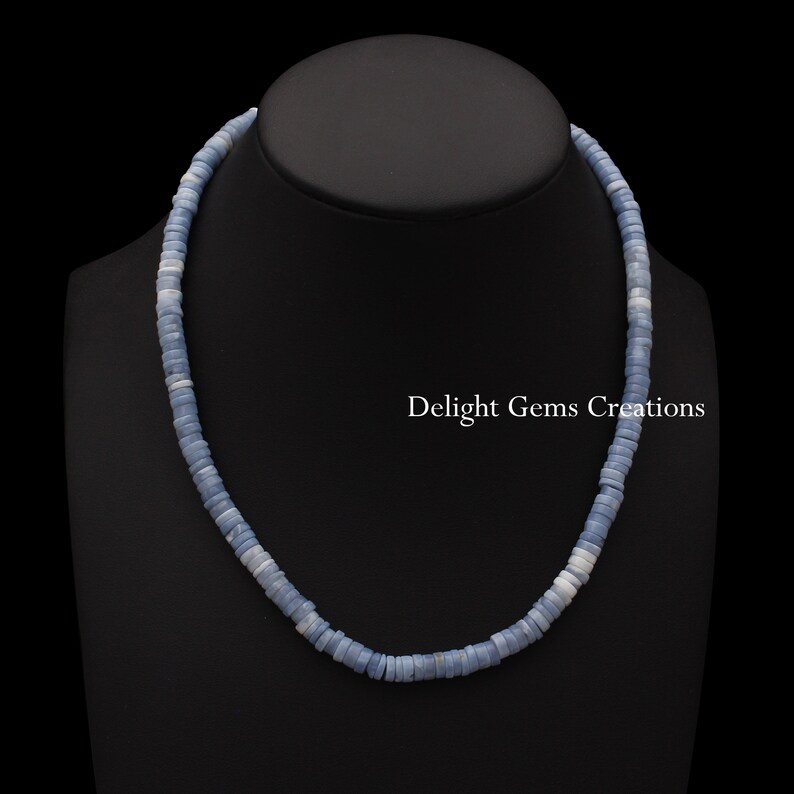 May include: A light blue opal bead necklace with a silver clasp. The necklace is on a black mannequin bust. The text "Delight Gems Creations" is visible in the image.