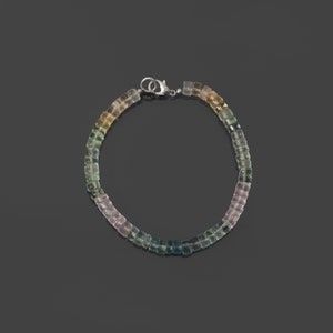 May include: A multi-colored gemstone bracelet with a silver clasp. The bracelet features a gradient of colors, starting with light pink, transitioning to green, and ending with a light yellow.