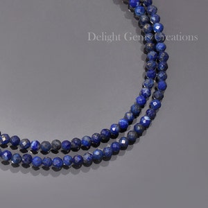 May include: A double strand necklace made of dark blue lapis lazuli beads. The beads are faceted and have a slightly metallic sheen. The necklace is on a grey background. Delight Gems Creations is printed on the background.