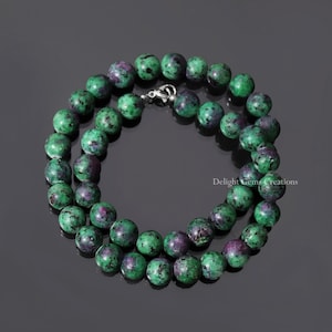 Puede incluir: Un collar de piedras preciosas verdes y moradas con cuentas redondas. El collar está hecho de piedras naturales y tiene un cierre de plata.