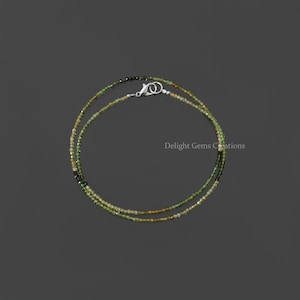 Peut inclure: Un collier délicat composé de perles de pierres précieuses vertes et dorées. Le collier est composé de deux rangs de perles et possède un fermoir argenté.