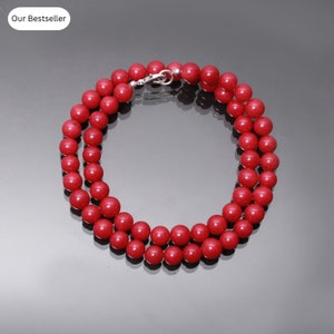 Puede incluir: Un collar de cuentas de coral rojo con un cierre de plata. El collar está hecho de cuentas redondas y tiene aproximadamente 45 cm de largo.