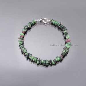 May include: A bracelet made of small, irregularly shaped green and red gemstones. The bracelet is strung together with a silver-colored clasp. The gemstones are a mix of dark green and red hues, creating a natural, earthy look.