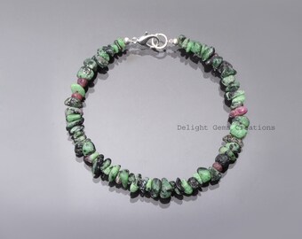 May include: A bracelet made of small, irregularly shaped green and red gemstones. The bracelet is strung together with a silver-colored clasp. The gemstones are a mix of dark green and red hues, creating a natural, earthy look.