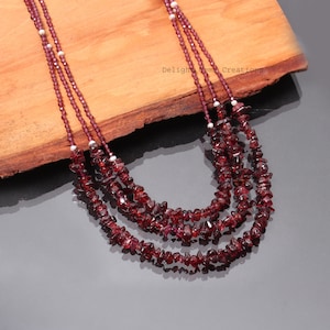 May include: A multi-strand necklace made of small, irregular red garnet beads. The necklace is layered with three strands of beads and features small white beads interspersed throughout.