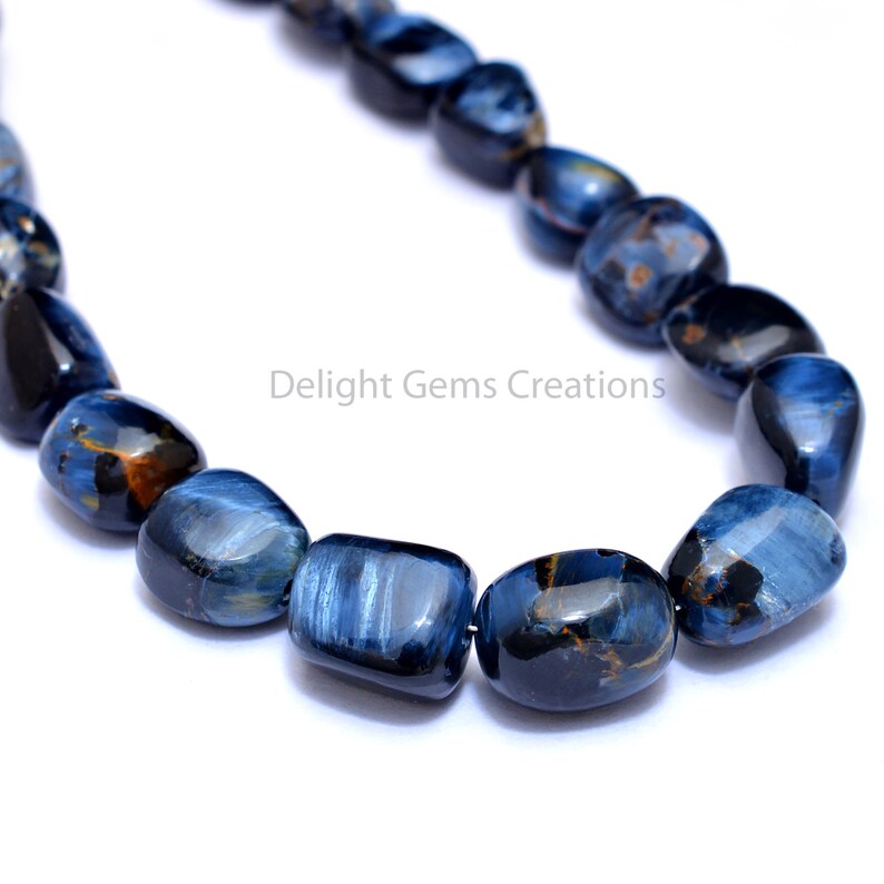 May include: A strand of blue tiger's eye gemstone beads, each bead is a smooth, rounded rectangle shape.