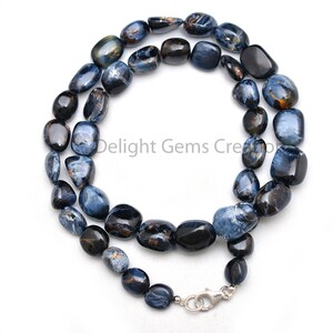 May include: A blue and black tiger's eye gemstone necklace with a silver clasp. The necklace is made of smooth, rounded beads.