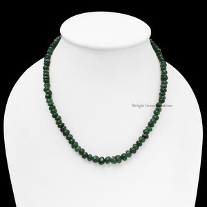Puede incluir: Un collar de peque&ntilde;as cuentas de piedras preciosas de color verde oscuro. Las cuentas son redondas y est&aacute;n ensartadas. El collar se exhibe sobre un maniqu&iacute; blanco, sobre un fondo negro. Una joya elegante.