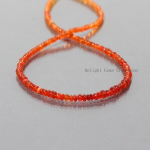 May include: A strand of orange opal beads, strung on a thin cord. The beads are small and round, and they have a slight shimmer to them.