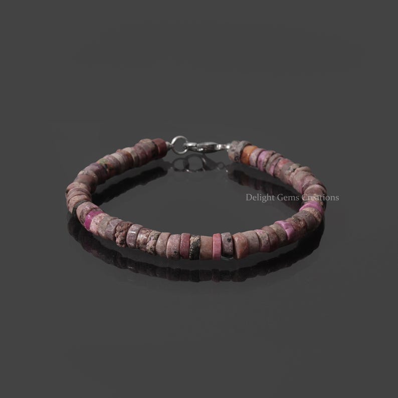 May include: A pink and brown beaded bracelet with a silver clasp. The bracelet is made of small, irregular shaped beads.