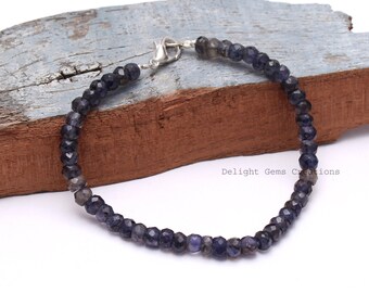 May include: A dark blue beaded bracelet with a silver clasp. The beads are faceted and have a deep indigo color. The bracelet is displayed on a wooden surface. The text "Delight Gems Creations" is visible.