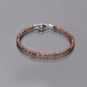 May include: A brown gemstone bracelet with a silver clasp. The bracelet is made of small, faceted gemstones that are strung together on a silver chain.