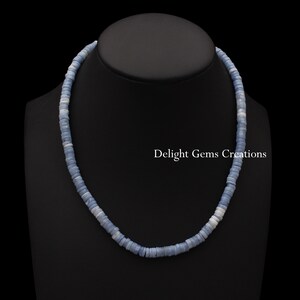 May include: A light blue opal bead necklace with a silver clasp. The necklace is on a black mannequin bust. The text "Delight Gems Creations" is visible in the image.