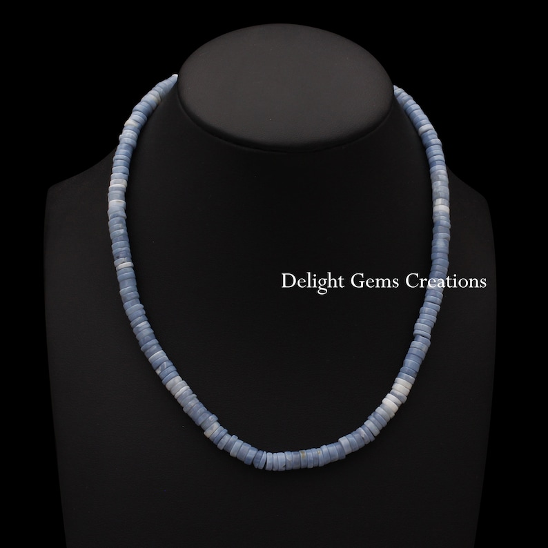 May include: A light blue opal bead necklace with a silver clasp. The necklace is on a black mannequin bust. The text "Delight Gems Creations" is visible in the image.