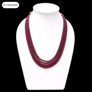 May include: A multi-strand necklace made of deep red beads. The necklace is displayed on a white mannequin bust.