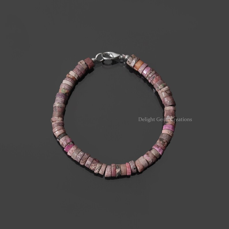 May include: A pink and white gemstone bracelet with a silver clasp. The bracelet is made of small, round beads.