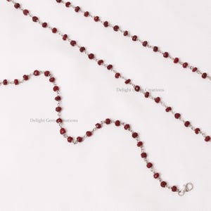 May include: Two silver chains with red gemstone beads. The chains are laid out on a white surface. The text "Delight Gems Creations" appears twice in the image.
