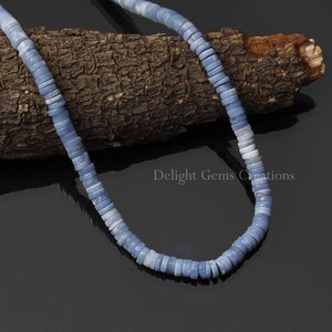 May include: A strand of light blue and white opal beads, arranged in a circle on a piece of wood. The beads are smooth and have a slightly iridescent sheen.