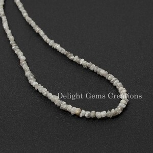 May include: A strand of rough, white diamond beads strung on a silver chain. The beads are irregular in shape and size, and they have a natural, unpolished look. The chain is delicate and has a simple design.