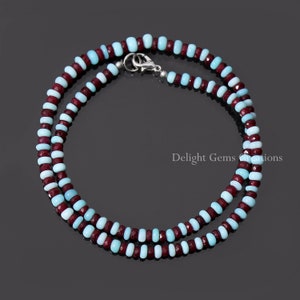 May include: A double-strand necklace made of alternating light blue and burgundy gemstone beads. The necklace has a silver clasp.