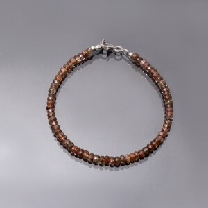 May include: A brown gemstone bracelet with a silver clasp. The bracelet is made of small, round beads.