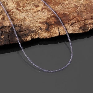 May include: A delicate necklace made of small, light purple beads. The necklace is displayed on a piece of rough-hewn wood.