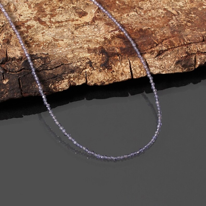 May include: A delicate necklace made of small, light purple beads. The necklace is displayed on a piece of rough-hewn wood.