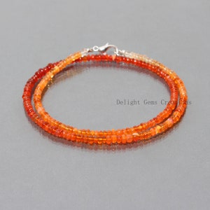 May include: A double strand necklace made with small, round, orange and red opal beads. The necklace is secured with a silver clasp.