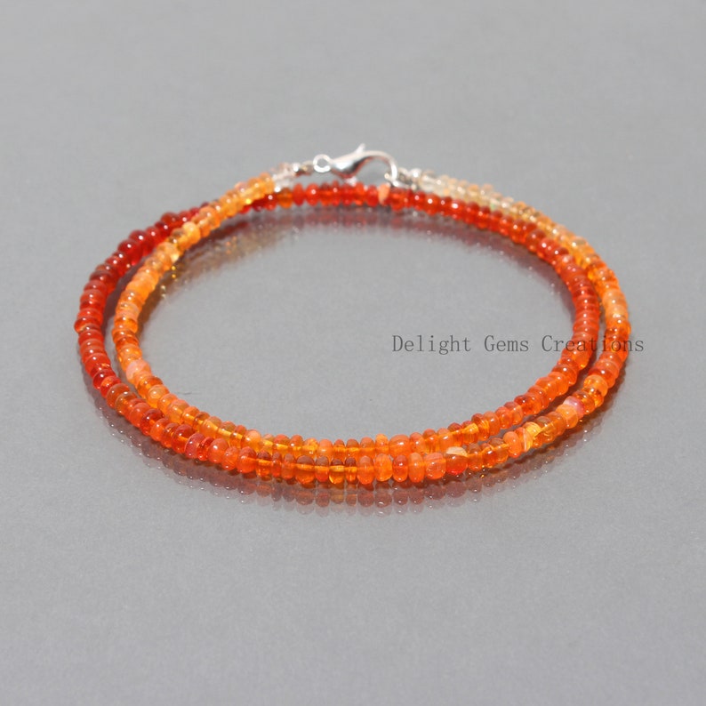 May include: A double strand necklace made with small, round, orange and red opal beads. The necklace is secured with a silver clasp.