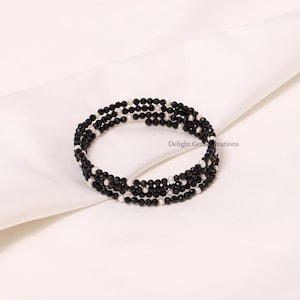 May include: A black and white beaded bracelet with multiple strands of black beads and white beads. The bracelet is wrapped around itself and is lying on a white surface.