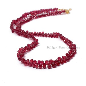 Può includere: Una collana con piccole gemme rosse scure sfaccettate. Le perline sono infilate in un motivo delicato, con una chiusura color oro. La collana è esposta su sfondo bianco. Il testo "Delight Gems Creations" è visibile.