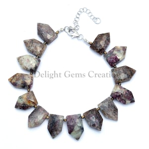 May include: A necklace made with faceted, pink and white, gemstone beads. The beads are in a pointed, teardrop shape. The necklace has a silver clasp.
