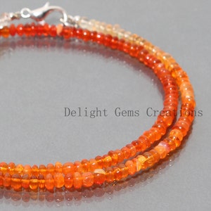 May include: A necklace made of orange and yellow opal beads. The necklace is made of two strands of beads and has a silver clasp.