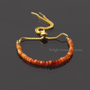 May include: A gold chain bracelet with a sliding clasp and a row of orange and red gemstone beads.  Delight Gems Creations.