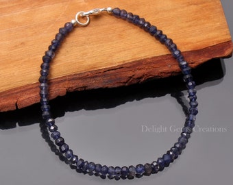 May include: A silver chain bracelet with dark blue faceted gemstone beads. The bracelet is on a wooden surface.