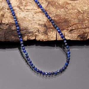 May include: A delicate necklace made with small, faceted, dark blue lapis lazuli beads. The necklace is displayed on a wooden surface.