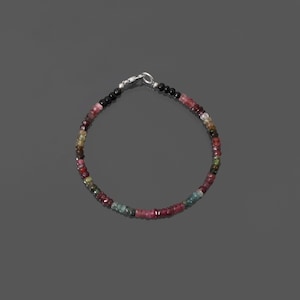 May include: A multi-colored gemstone bracelet with a silver clasp. The bracelet is made of small, round beads in shades of pink, green, and black.
