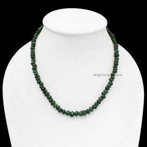 Puede incluir: Un collar de peque&ntilde;as cuentas de piedras preciosas de color verde oscuro. Las cuentas son redondas y est&aacute;n ensartadas. El collar se exhibe sobre un maniqu&iacute; blanco, sobre un fondo negro. Una joya elegante.