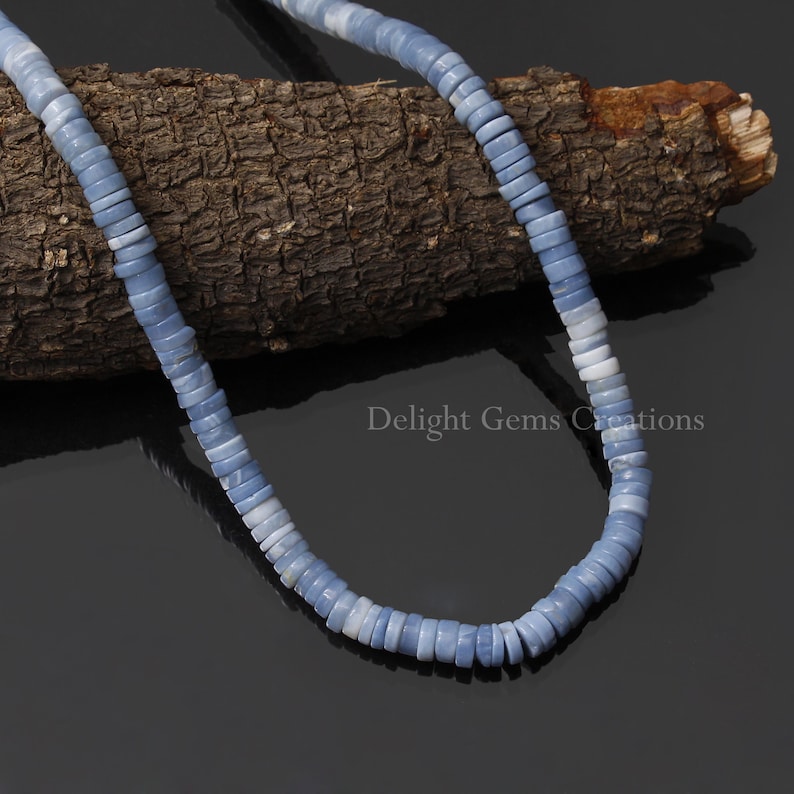 May include: A strand of light blue and white opal beads, arranged in a circle on a piece of wood. The beads are smooth and have a slightly iridescent sheen.