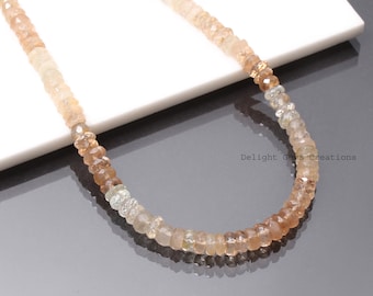 May include: A long necklace made of light brown, tan, and clear faceted gemstone beads. The necklace is on a white surface with the text "Delight Gems Creations" in the lower right corner.