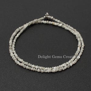 May include: A silver necklace made of small, rough, white diamonds. The necklace is made of two strands of diamonds and has a silver clasp.