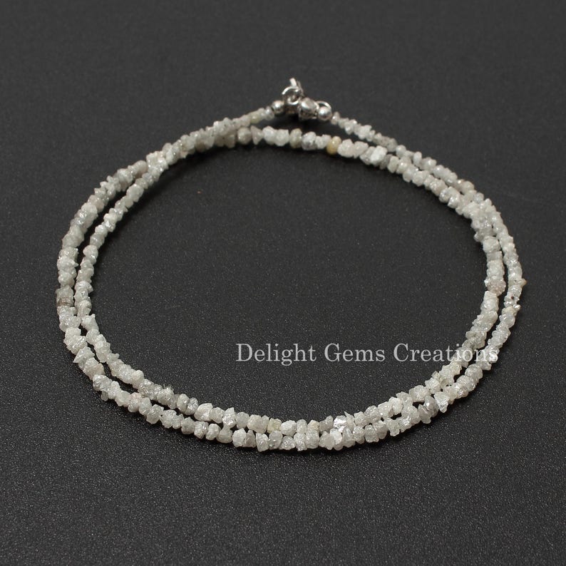 May include: A silver necklace made of small, rough, white diamonds. The necklace is made of two strands of diamonds and has a silver clasp.